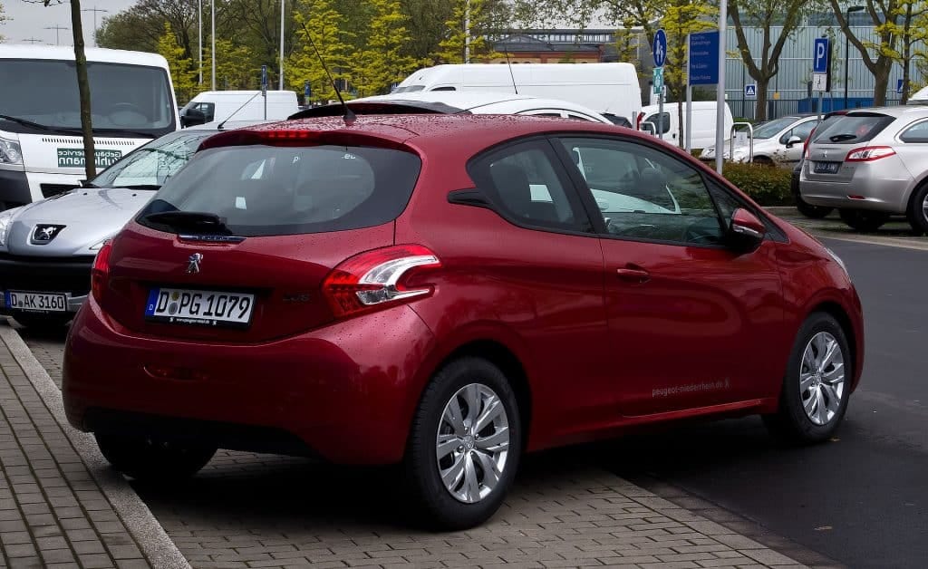 A red Peugeot 208 car parked on the side of the road with an Engine Oil Pressure Fault.