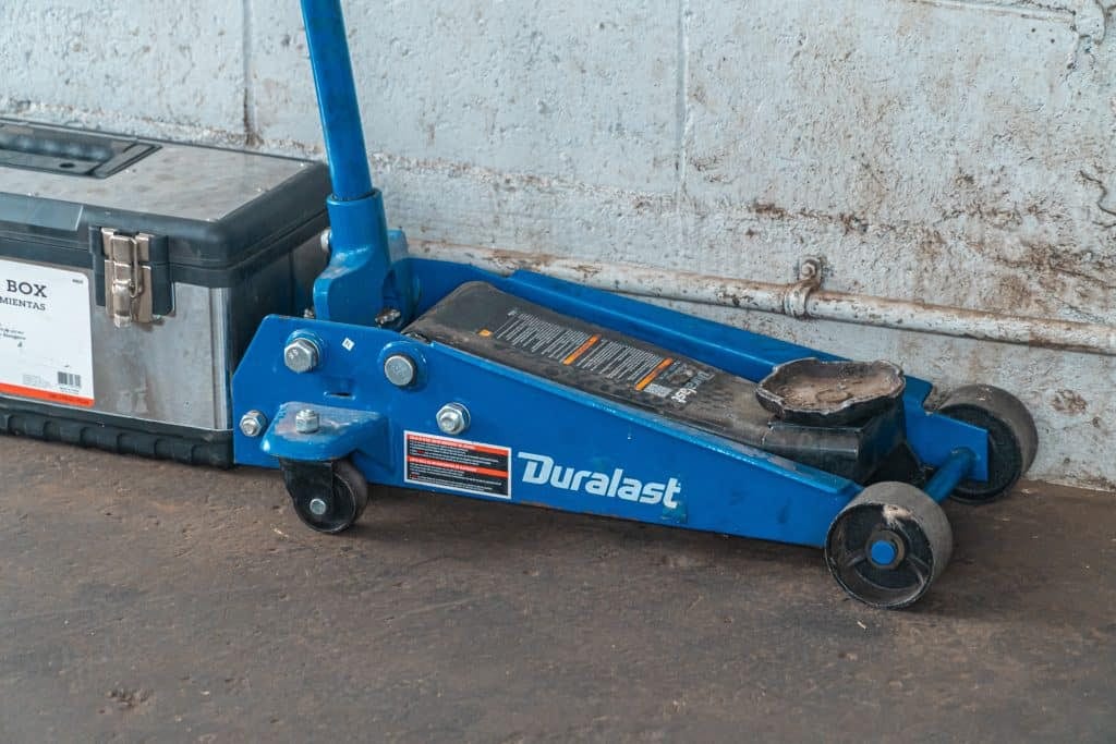 A blue floor jack with a tool box next to it.